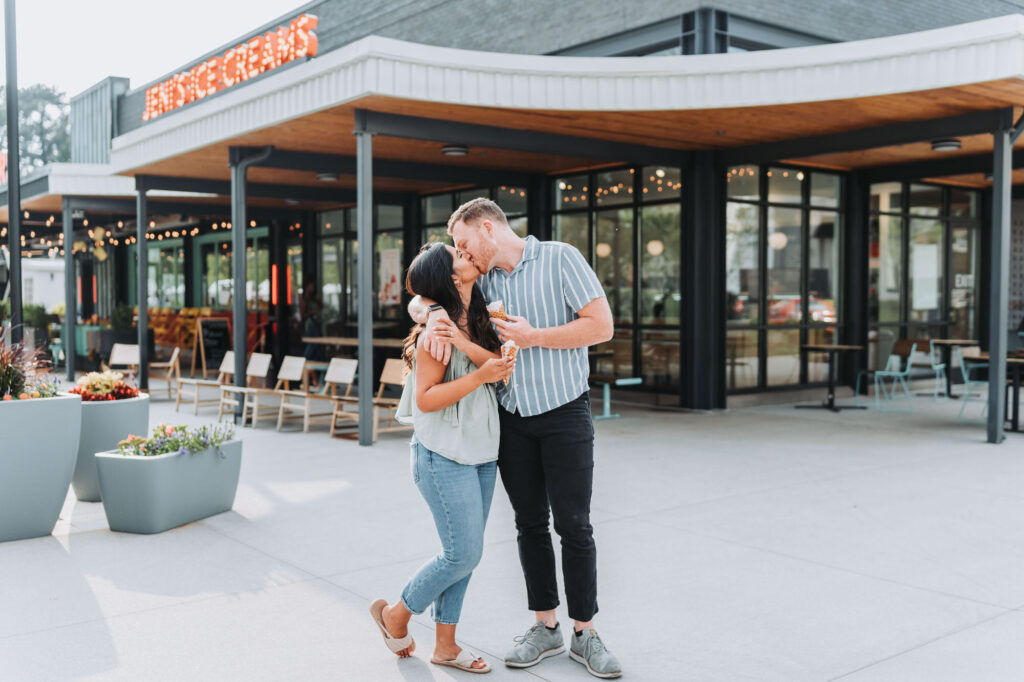 Couple holds ice cream cones and kisses in front of Jeni's ice cream in Atlanta, GA.