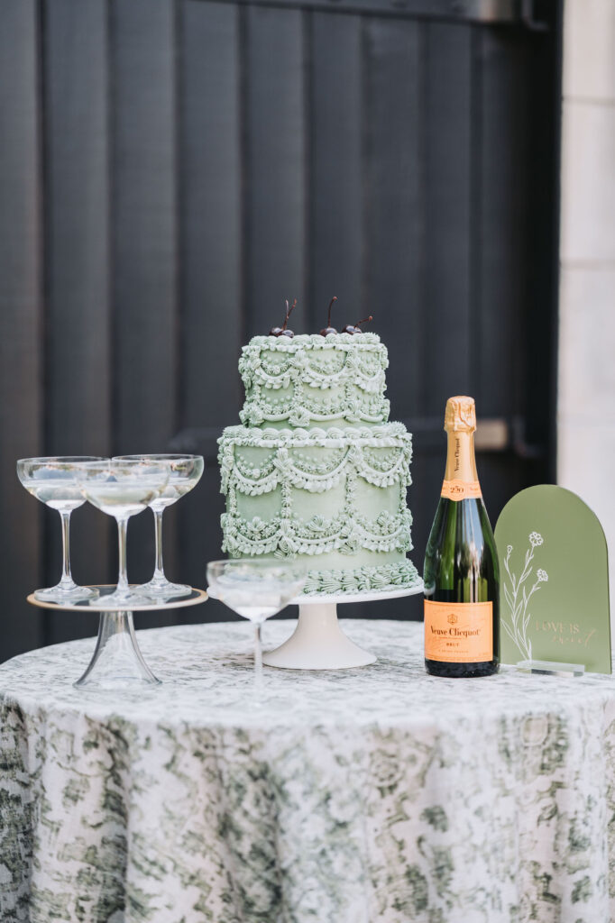 Wedding cake, champagne tower, and champagne bottle sit on wedding table. Wedding at Harper Fowlkes house in Savannah, GA.