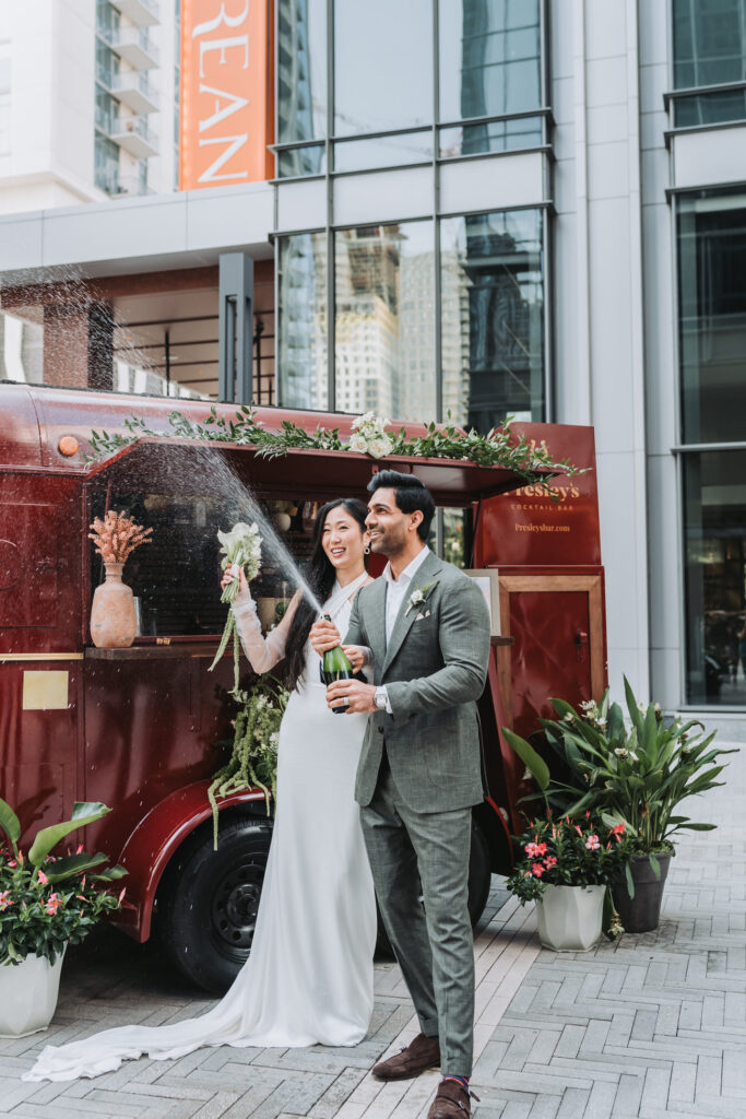 Bride and groom pop champagne with Bar cart in background at Epicurean hotel in Atlanta, GA.