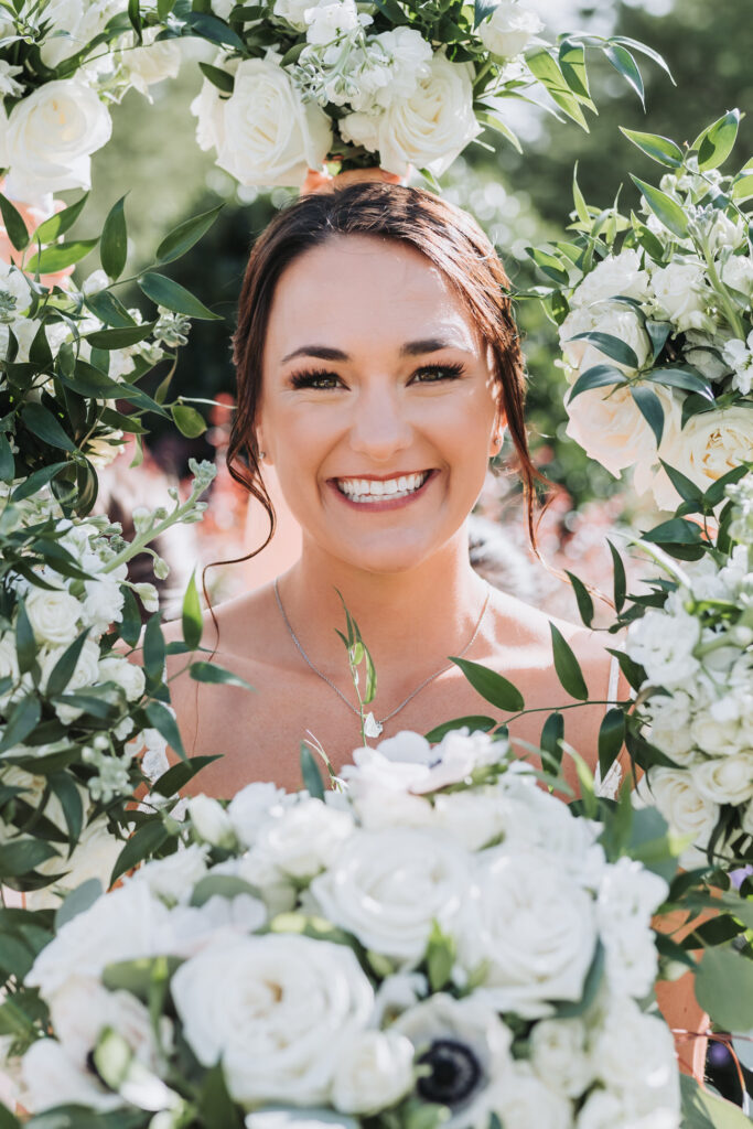 Bride smiles at camera with flower bouquets around her.