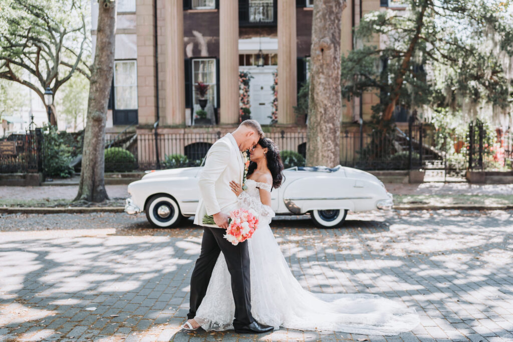 Bride and Groom pose outside of Harper Fowlkes House with a vintage car in the background.