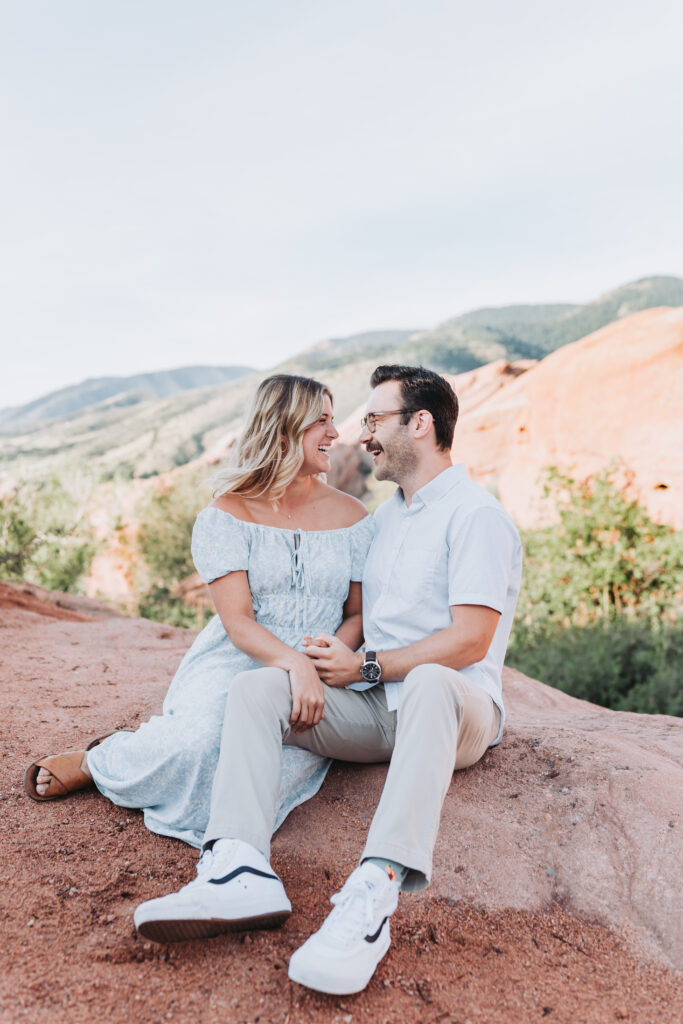 Couple sitting on mountain side during their red rock park engagement session in Colorado. 