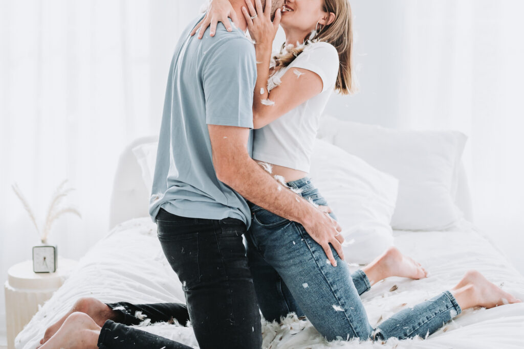 woman and man kiss on bed after their pillow fight engagement session