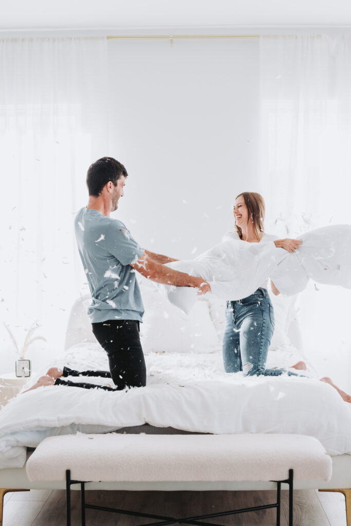 woman and man have pillow fight during their unique engagement shoot