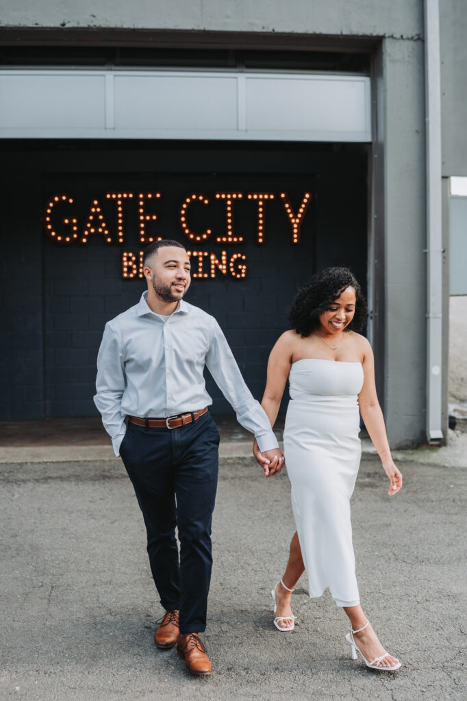 Couple walks towards camera with the Gate City Brewing sign behind them.