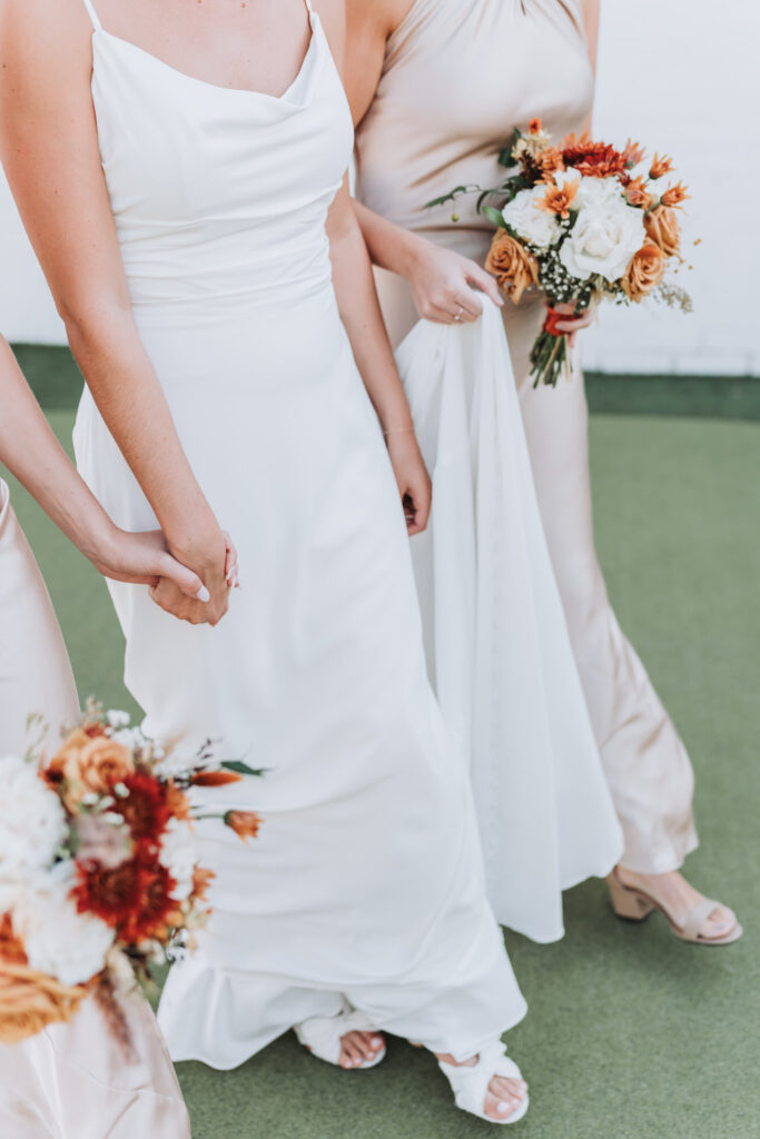 bride and bridesmaids hold hands while walking with fall bouquets.