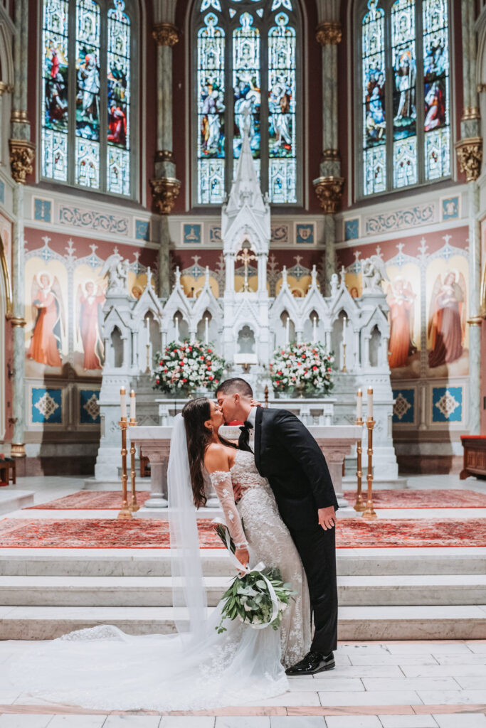 Groom kisses bride at the altar of Cathedral Basilica of St. John the Baptist wedding venue.