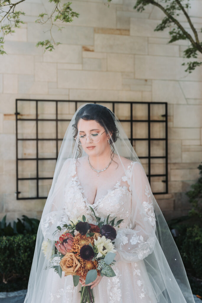 Bride has veil over her face and looks at her bouquet