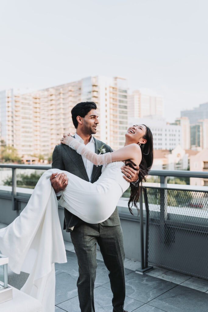 Groom picks up bride on terrace of epicurean hotel with the Atlanta city view in the background.