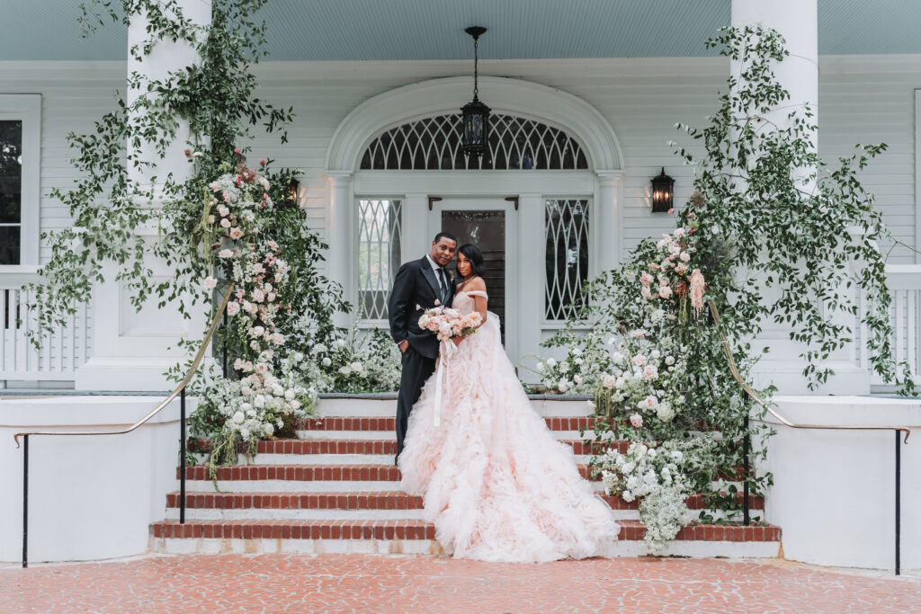 Bride and groom pose in front of their wedding ceremony site at the Admirals house in Charleston, SC. Bride wears a pink wedding dress from The Bridal House of Beaufort.