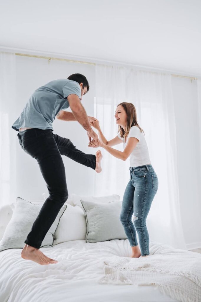 Engaged couple jumping on bed during photoshoot