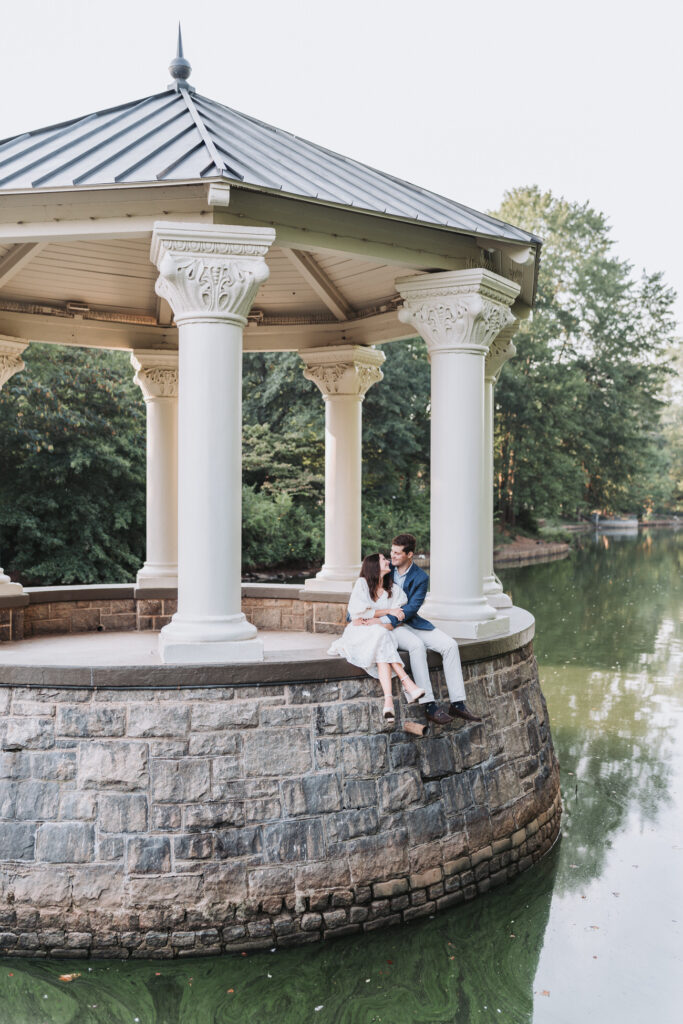 girl and guy hold each other while sitting on the edge of a gazebo at piedmont park.