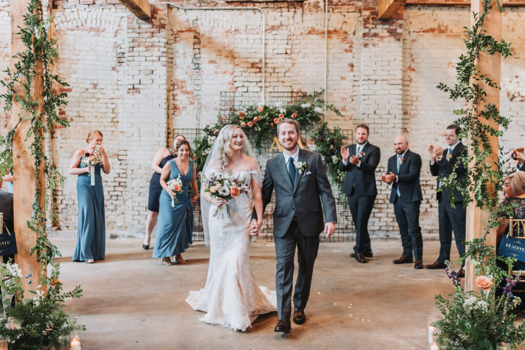 Bride and groom walks down the wedding aisle as they hold hands 