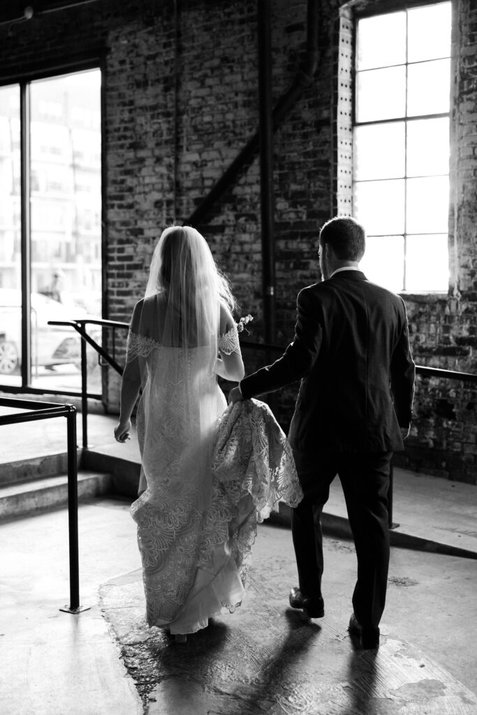 Groom holds bride's dress as they walk together