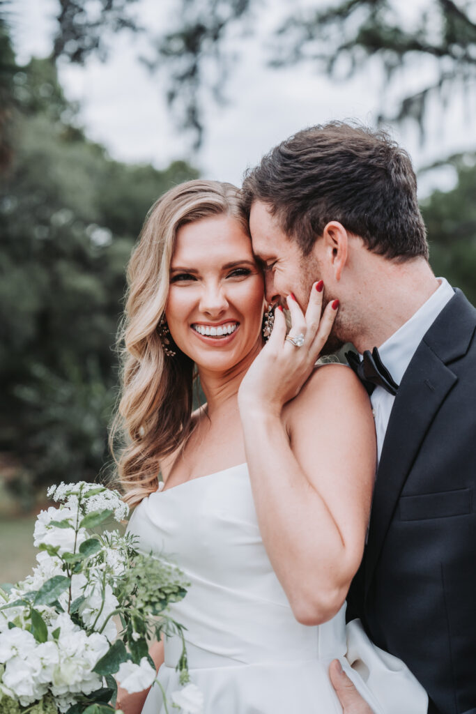Bride holds grooms face as he whispers in her ear