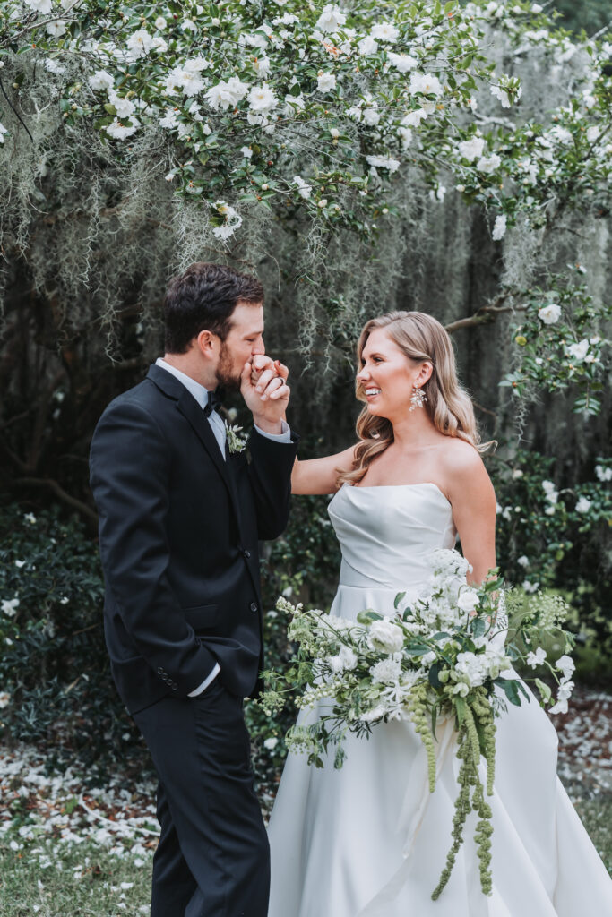 Groom kisses bride's hand under floral bush