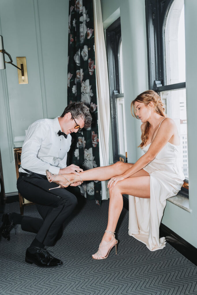 man ties the straps of woman's shoes for their engagement photos