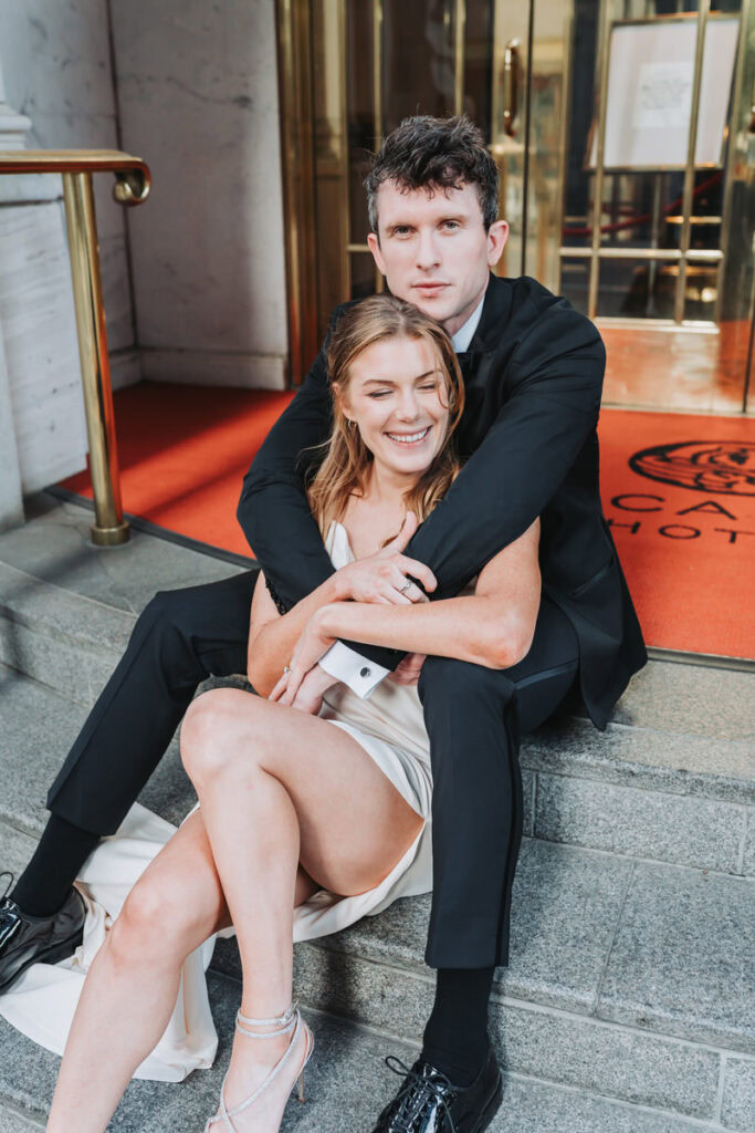 guy hugs girl from behind and looks at camera.