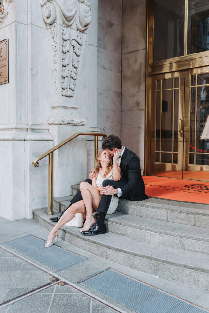 Girl and guy sit on stairs outside of Candler Hotel. She touches his face and pulls him in for a kiss.