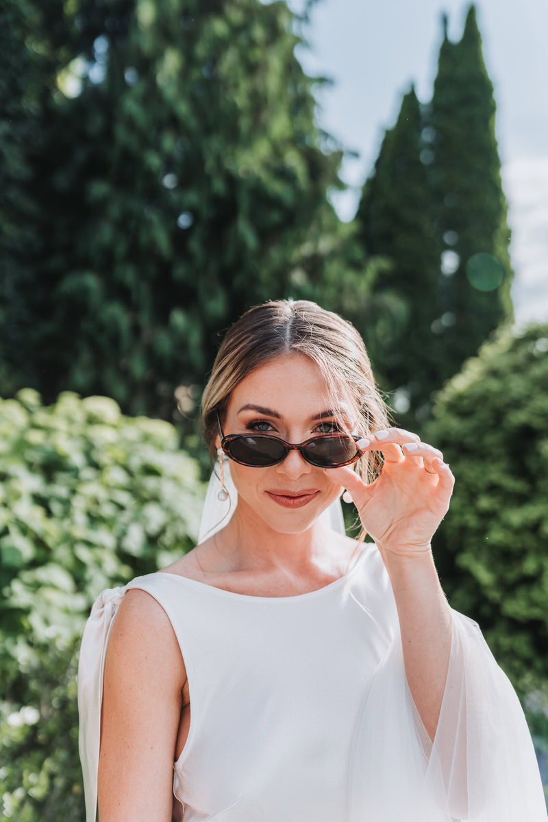 Bride looks at camera and peeks through her sunglasses.