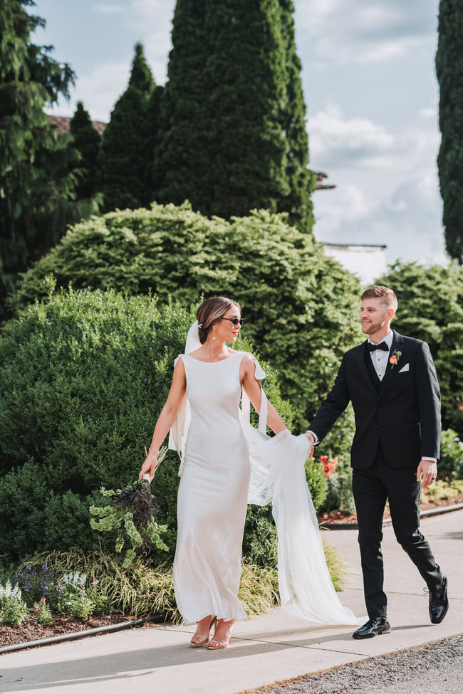 groom holds bride's veil while they walk.