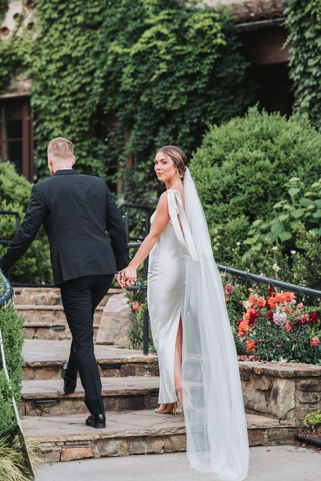 bride looks at the camera while holding grooms hand.