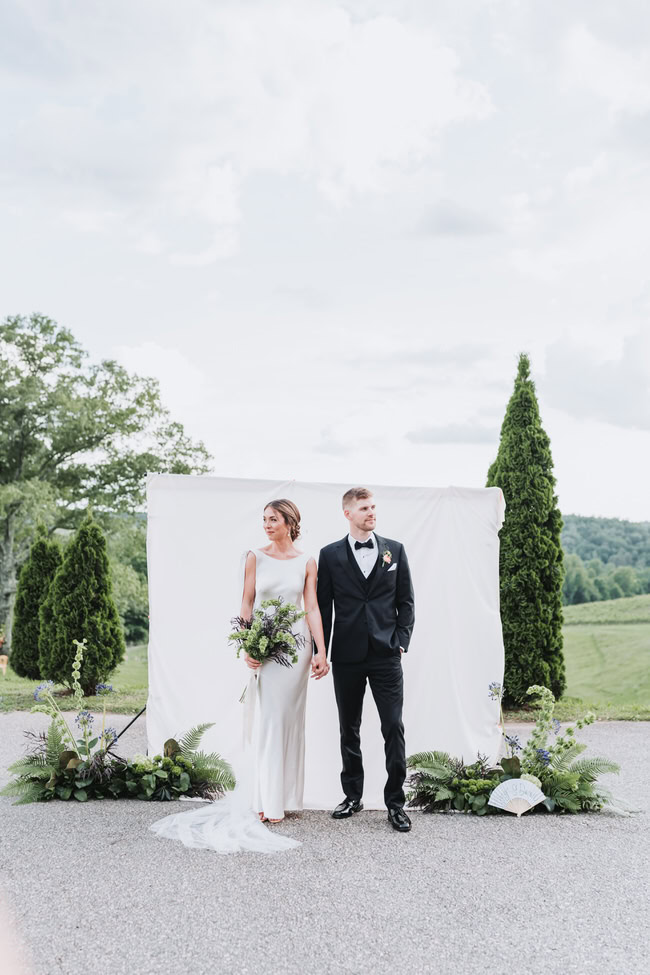 bride and groom hold hands in front of white sheet backdrop.