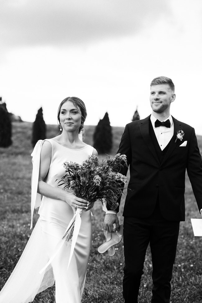 bride and groom look off towards the venue while holding hands.