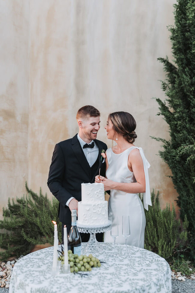 bride and groom laugh at each other while cutting their wedding cake