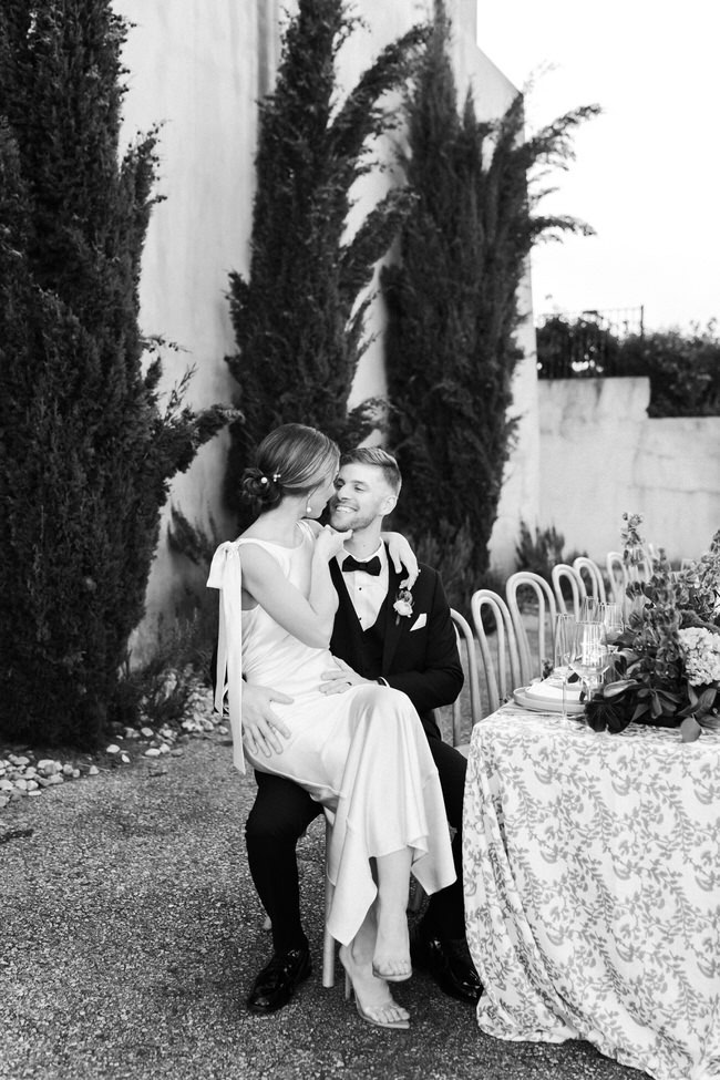 bride sits on groom's lap at the wedding reception table.