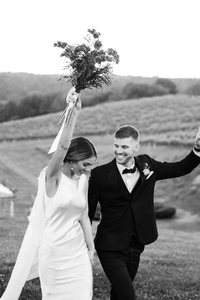 bride throws her bouquet in the air while they walk down their wedding aisle. 