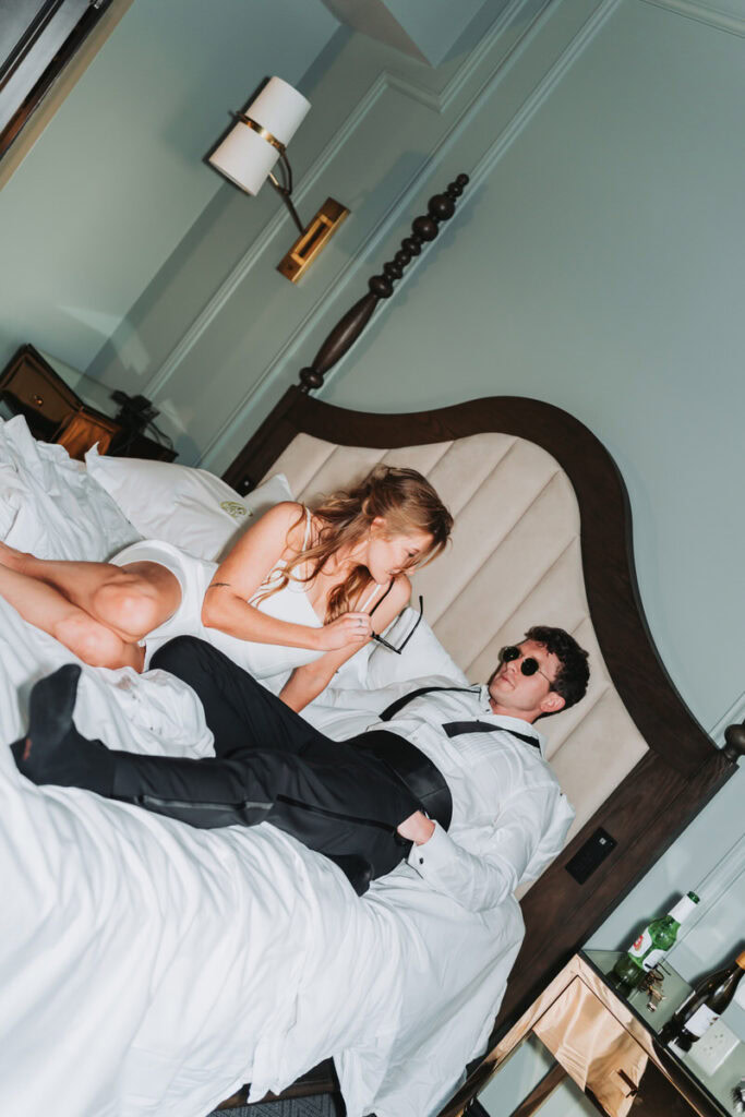 girl and guy wear sunglasses on the bed as they look at each other