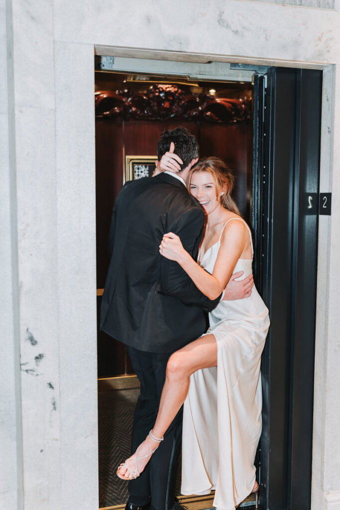 girl and guy take photos in the elevator. She wraps her leg around him.