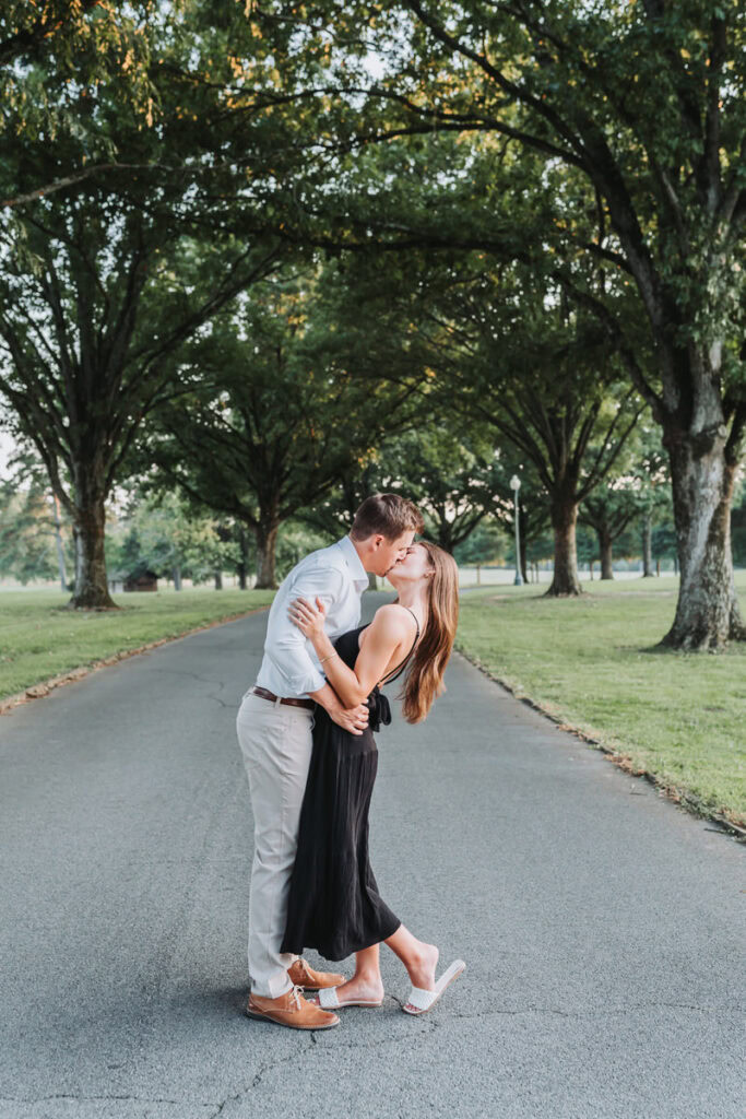 guy dips girl back and kisses her in front of the long line of oak trees