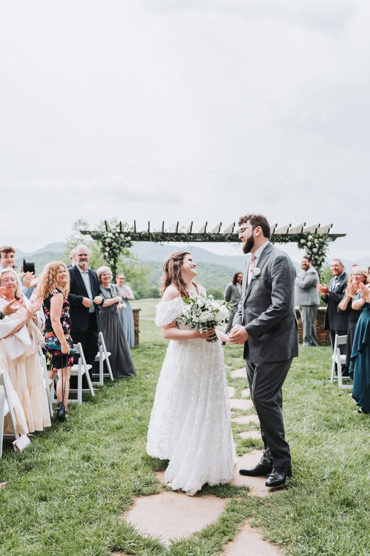 bride and groom look at each other as they walk down the aisle