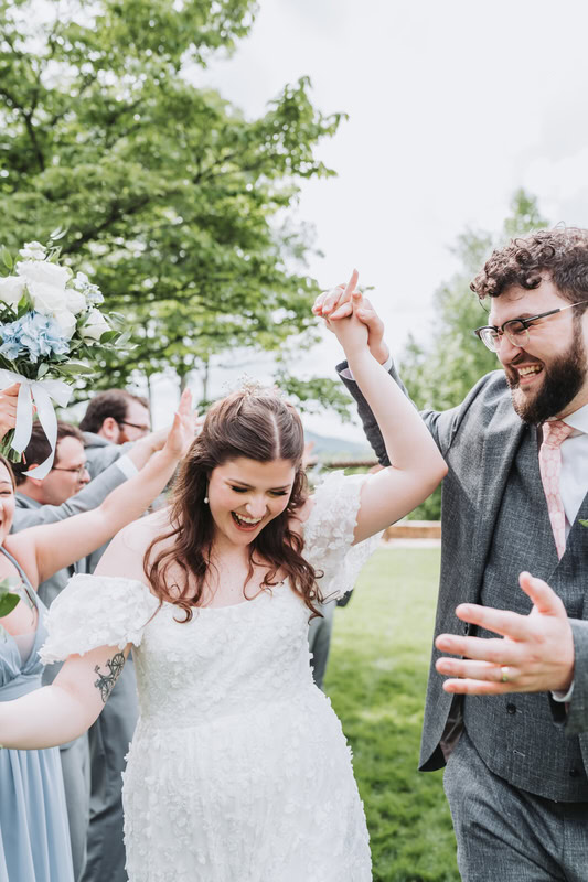 groom holds up bride's hand as they walk past their wedding party