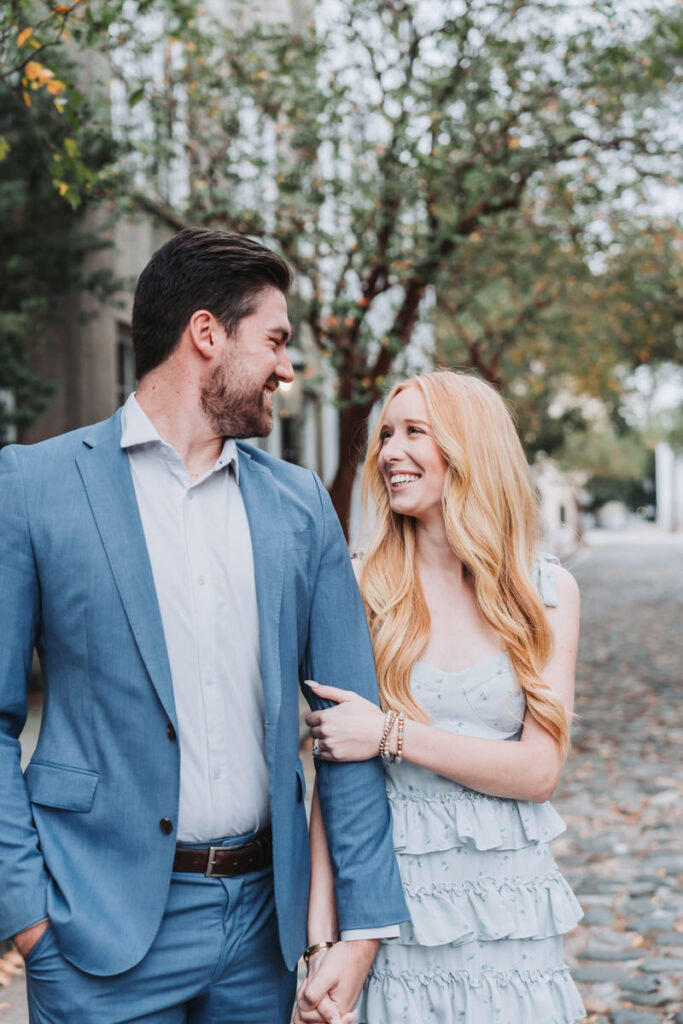 girl holds guys hand as they walk in downtown charleston for their engagement session.