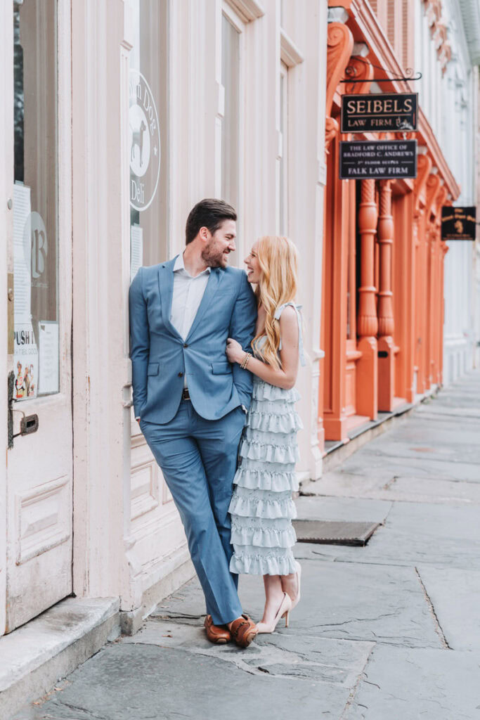 girl holds guys arm as he leans against a door frame in historic downtown Charleston