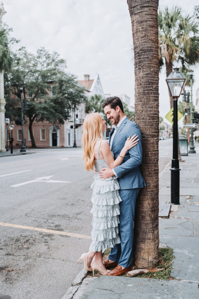 Guy leans against palm tree and girl leans against guy