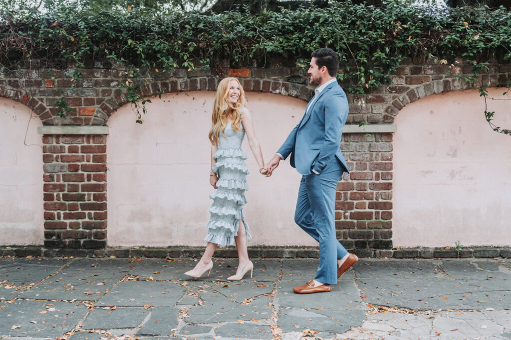 girl holds guys hand as they walk in downtown charleston for their engagement session.