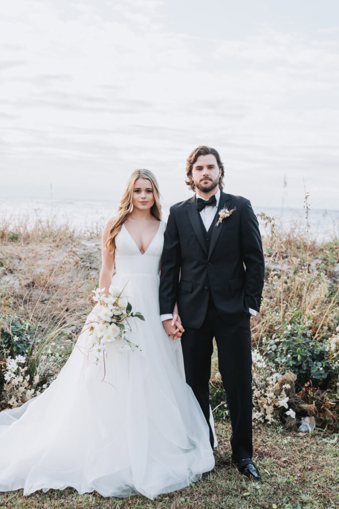 Bride and groom holds hands and looks at camera during Charleston beach elopement 