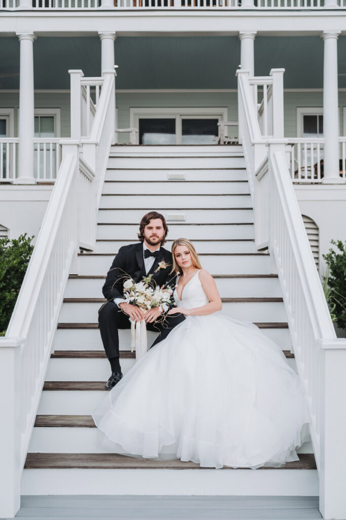 Bride and groom sit on step at beach house wedding venue