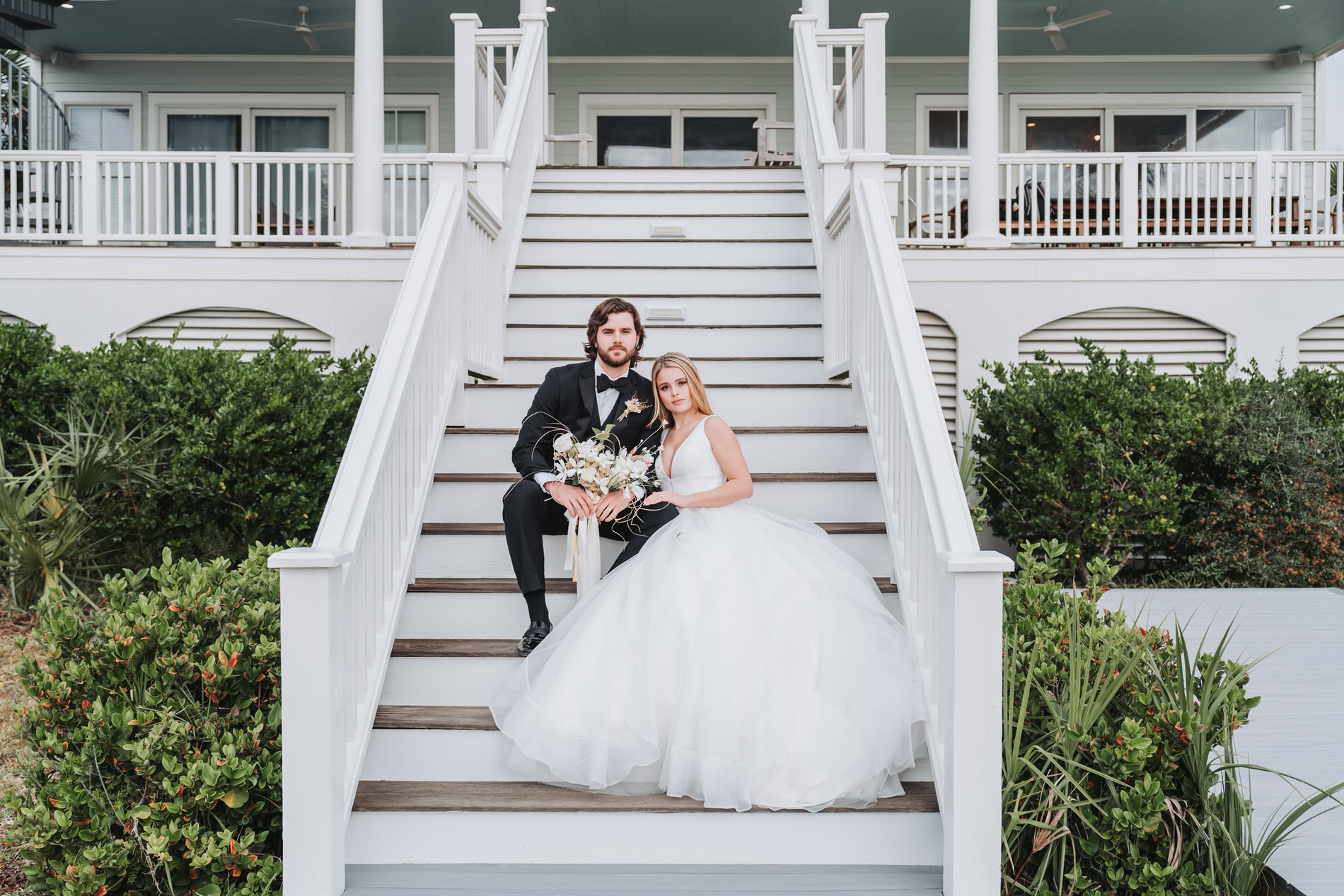 Bride and Groom sit on beach house stairs for their wedding portraits