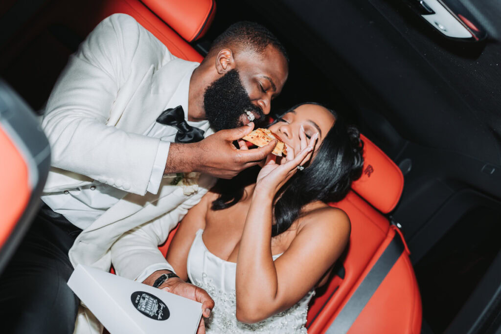 Bride and groom eat pizza in their Rolls royce for their wedding exit